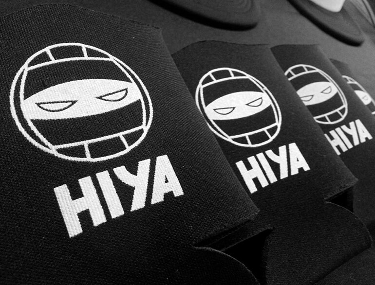 Three black koozies that have icon of volleyball combined with ninja eyes and HIYA text underneath printed on them